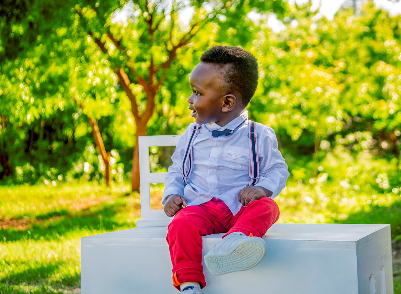 Adorable child seated outdoors in colorful attire, captured in a candid moment.